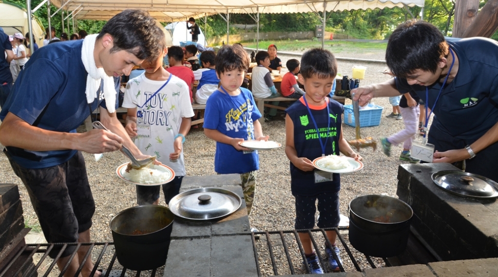 野外学習で子どもがカレーの配膳に並んでいる写真