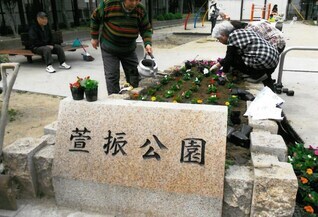 写真：萱振公園の石銘板の奥にある花壇で市民が手入れをしている