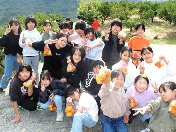 写真：お土産のみかんを手に記念撮影する児童ら