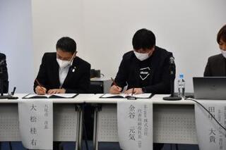 写真:協定書にサインする金谷社長と大松市長