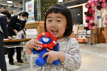 写真：ミャクミャクのぬいぐるみを手に取って笑顔の女の子