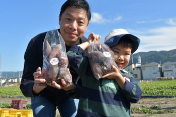 袋詰めしたさつまいもを手にする親子
