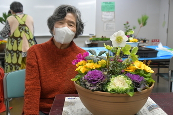 ハボタンを前に置いた作品とそれ作った女性