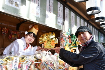 金色の縁起物を福娘から受け取る男性