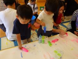 色のついた氷で模造紙におえかきをしている子どもの姿