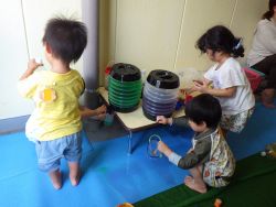 給水器に入れた色水をコップや容器に注いで楽しむ子どもたちの姿