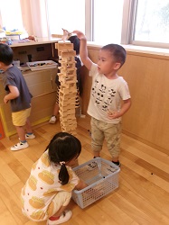 木の積み木カプラをタワーのように高く積みあげている子ども2人の様子。