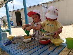 園庭の砂を使ってご飯作りをしている子どもの写真