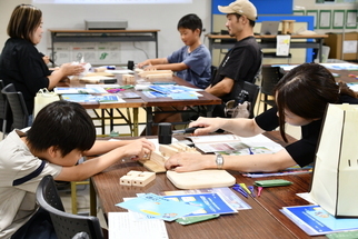 保護者と向かい合い、木製スツールを作り上げる子ども