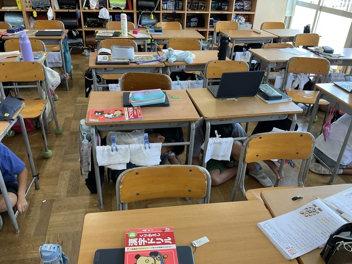 机の下に隠れる児童