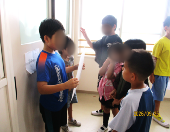 廊下でお店の説明を聞く子どもたち。高学年が低学年のお客さんへ向けて、画用紙に描いた案内を見せながら、口頭で説明している。